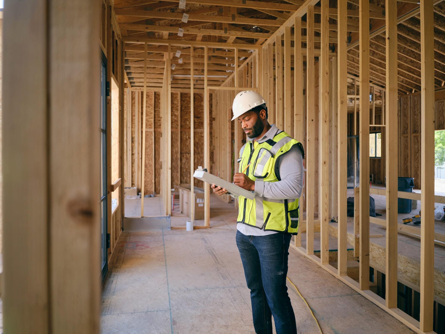 Building inspector with hard hat and hi-vis vest reviewing a clipboard inside a custom home during the framing inspection stage