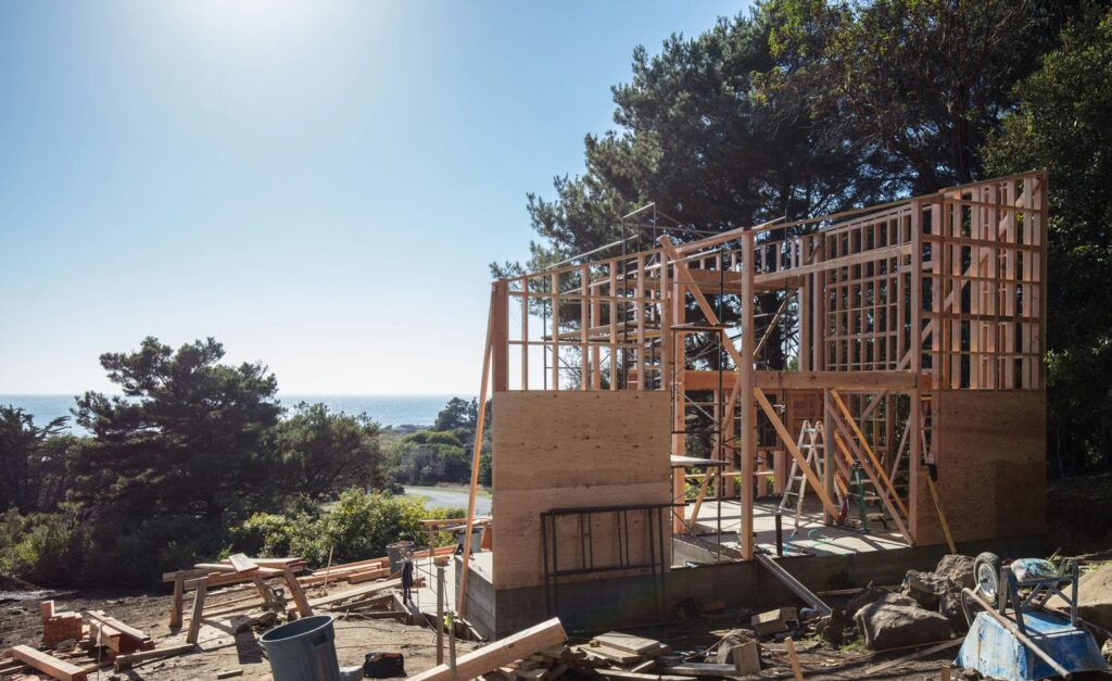 Custom home mid-build with partially framed walls and sheathing representing the residential framing process from sill plate to roof