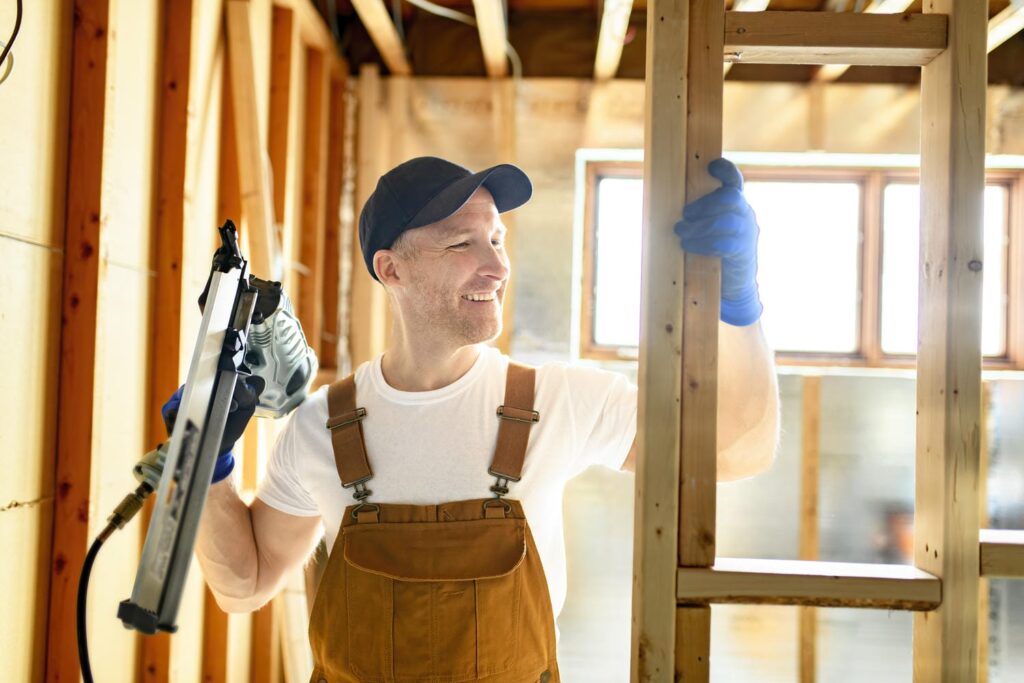 Framer holding a pneumatic nail gun while installing dimensional lumber wall studs during custom home wood frame construction
