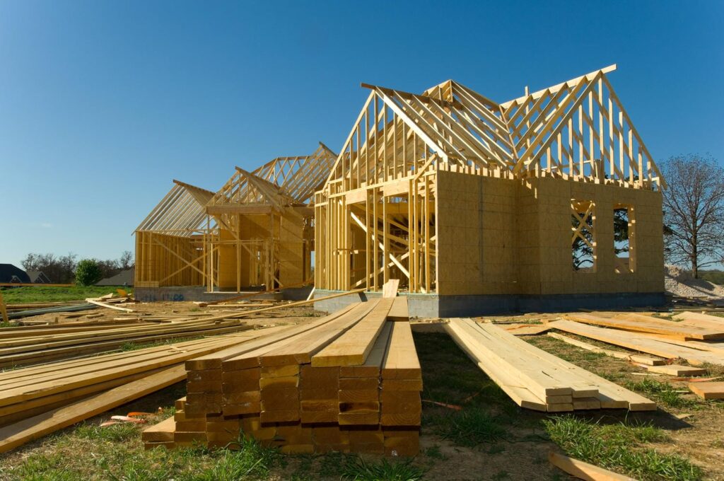 Custom home in the framing stage with wood roof trusses, sheathed walls, and stacks of dimensional lumber on site