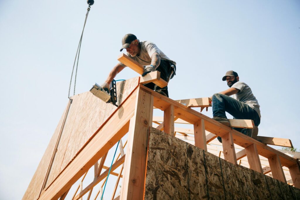 Two framing crew members working together to install roof sheathing and structural members on a custom home before a framing inspection
