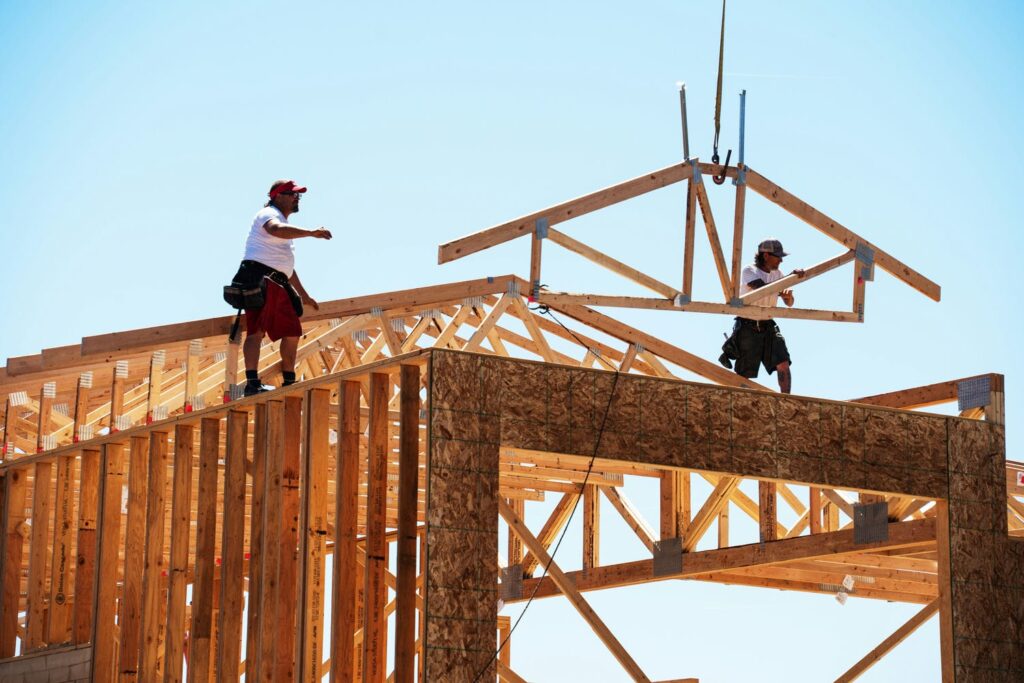 Framers installing pre-engineered roof trusses with a crane during custom home framing
