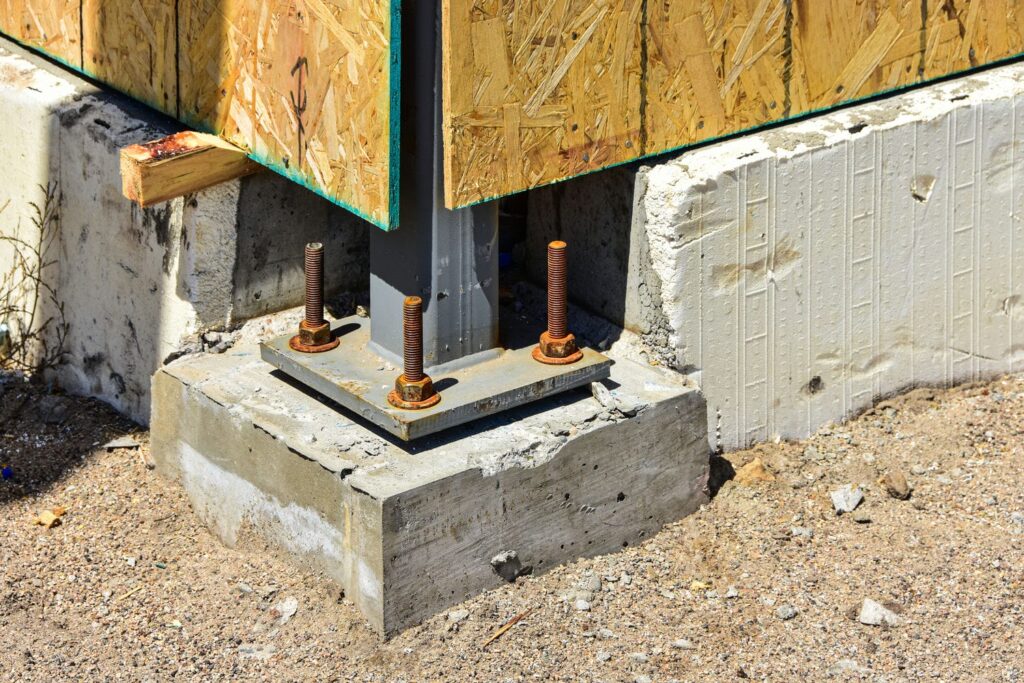 Anchor bolts and base plate securing a structural column to a concrete footing where framing meets the foundation