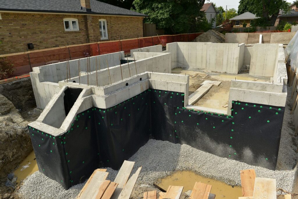 Custom home foundation with dimpled waterproofing membrane and perimeter drainage gravel installed connecting the foundation to framing readiness