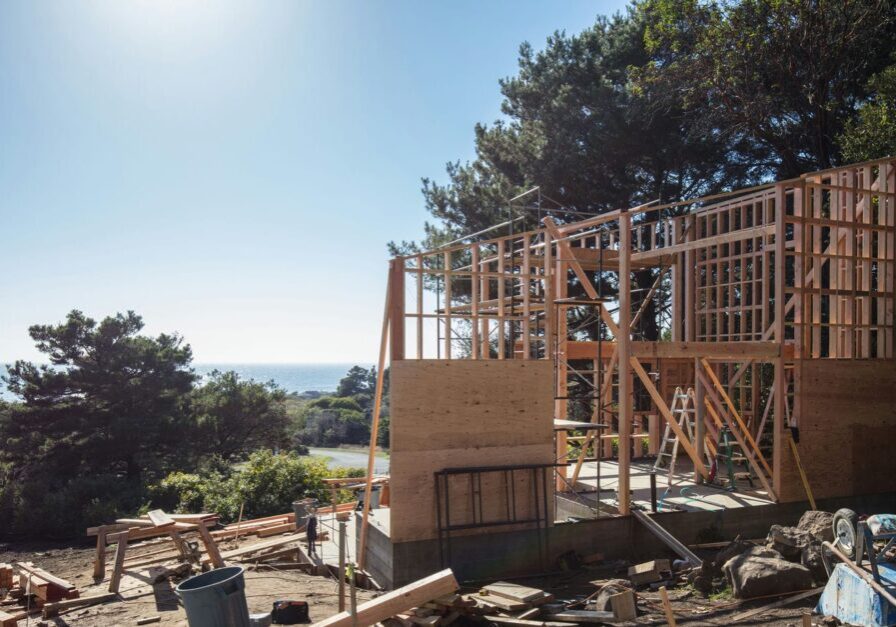 Custom home mid-build with partially framed walls and sheathing representing the residential framing process from sill plate to roof